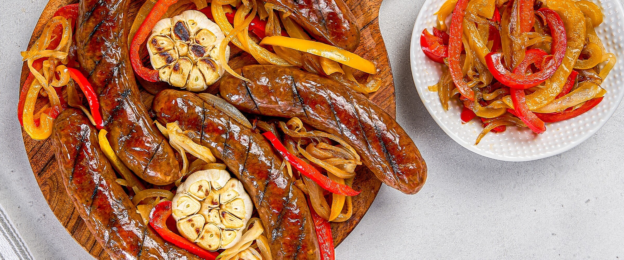 Close-up of a board of smokies, cooked bell peppers and roasted garlic.