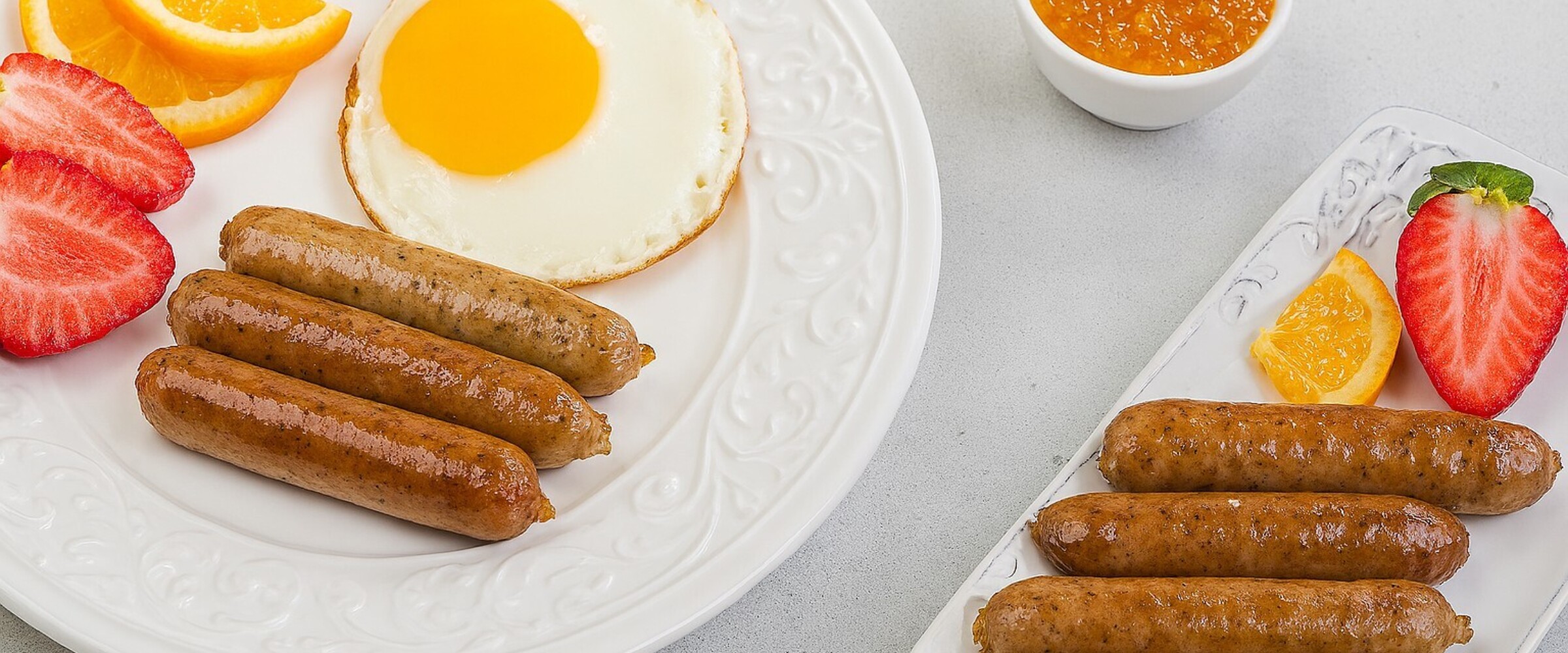 Close-up of a plate of breakfast sausages, eggs and fruit.