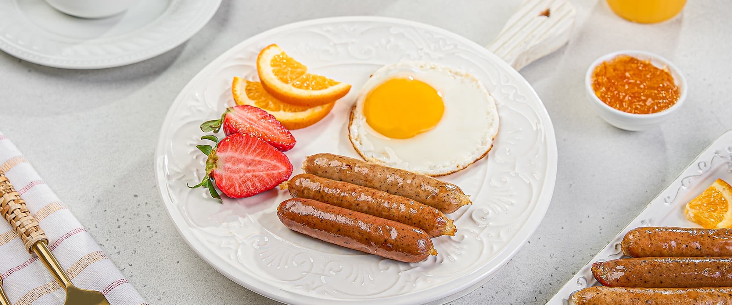 Close-up of a plate of breakfast sausages, eggs and fruit.