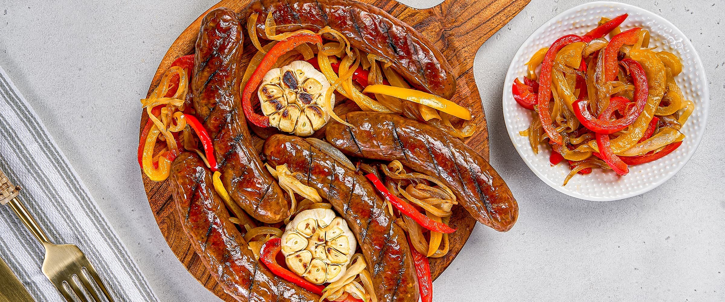 Close-up of a board of smokies, cooked bell peppers and roasted garlic.