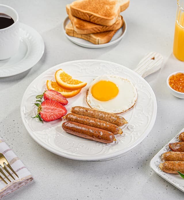 Close-up of a plate of breakfast sausages, eggs and fruit.