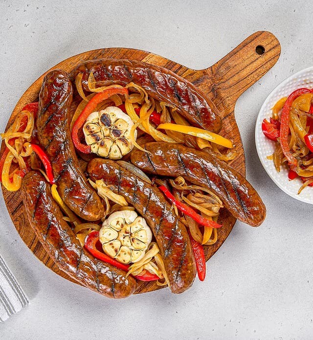 Close-up of a board of smokies, cooked bell peppers and roasted garlic.