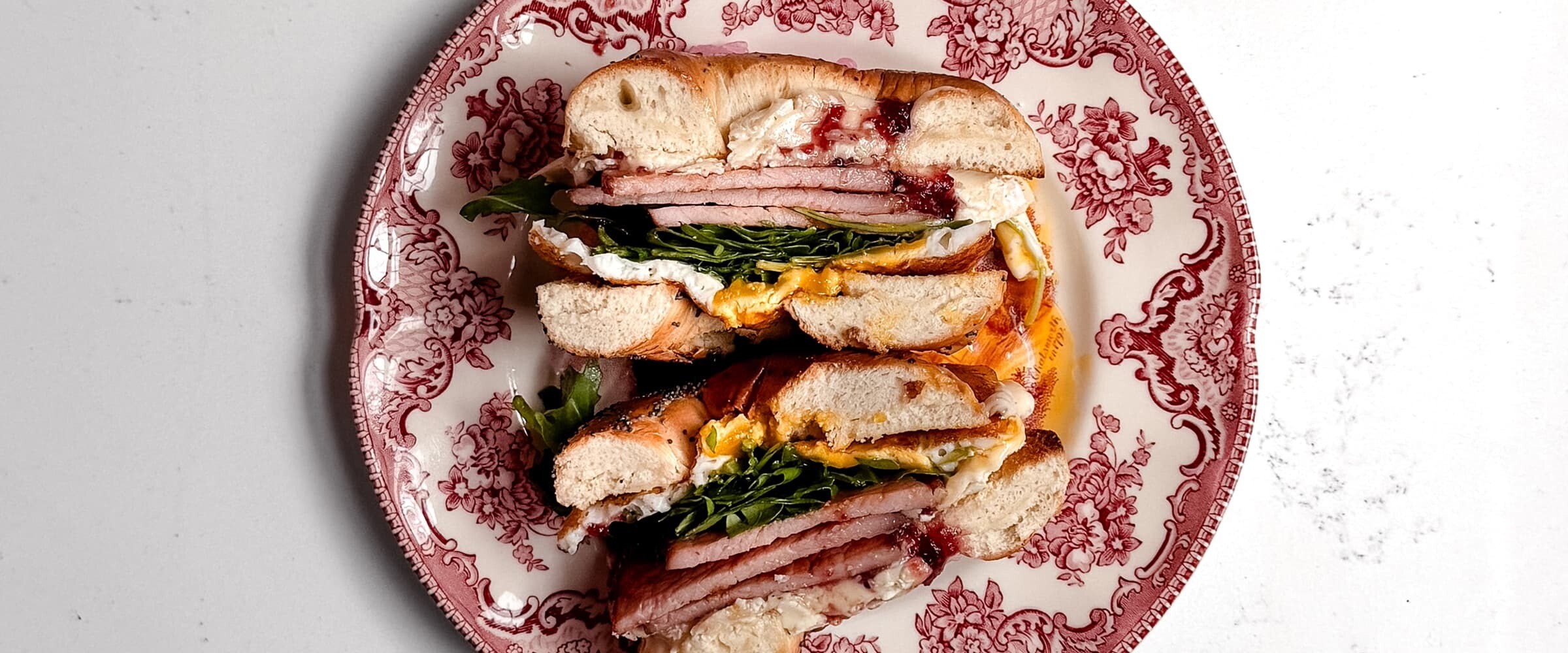 A close-up of a bacon sandwich cut in half and served on a decorative plate.