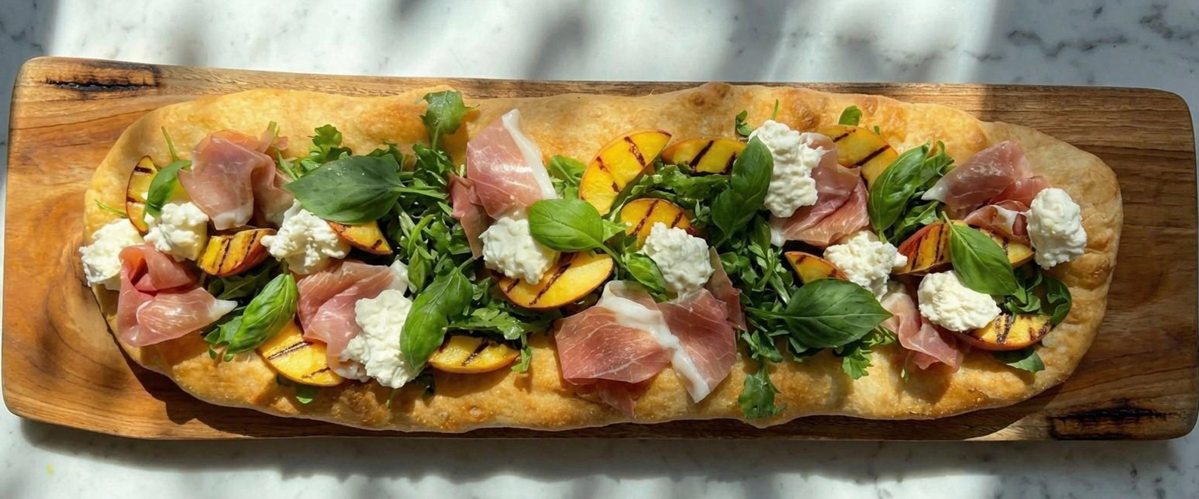 Une photo d'une Pinsa aux peches grillees et prosciutto