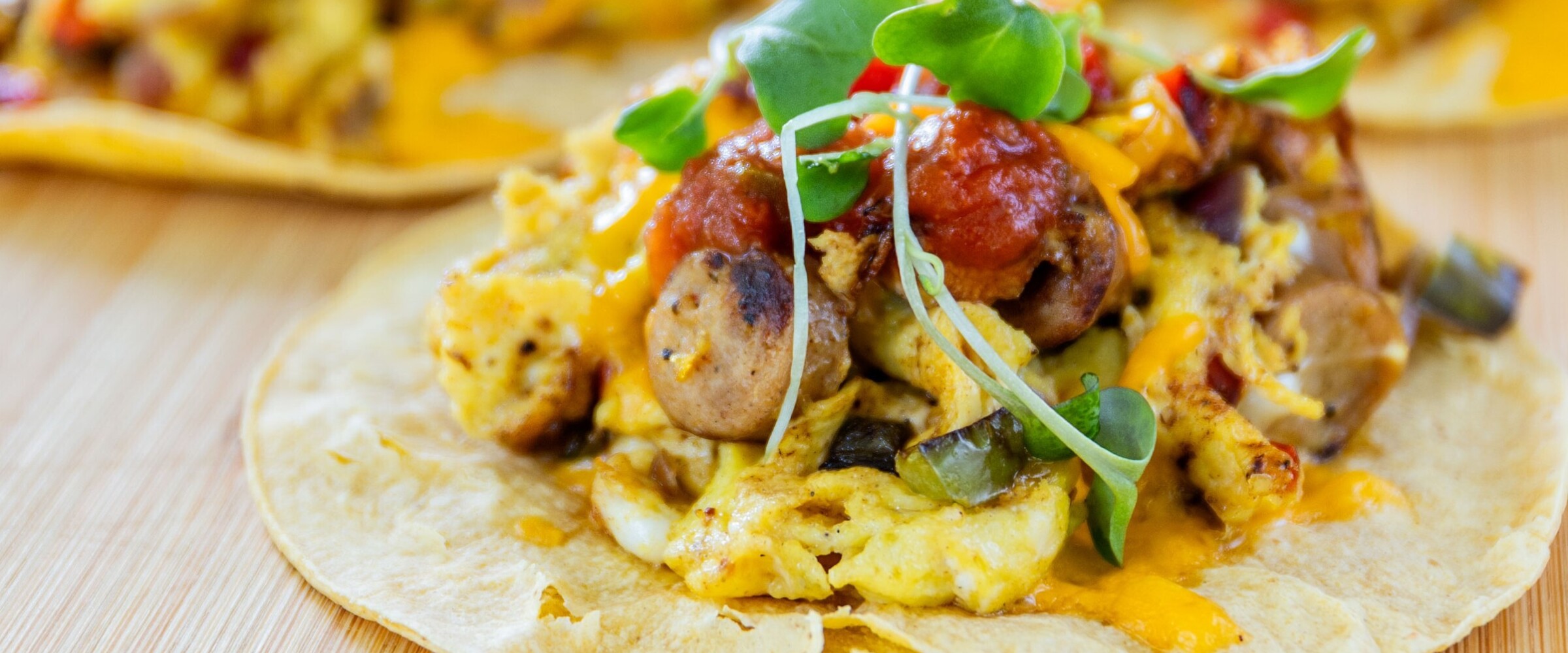 A close-up of 4 tacos plated on a wooden board.