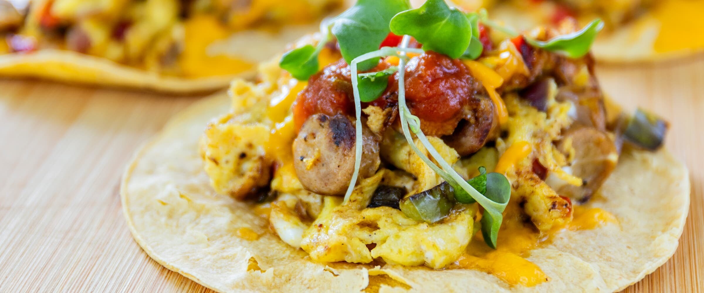 A close-up of 4 tacos plated on a wooden board.