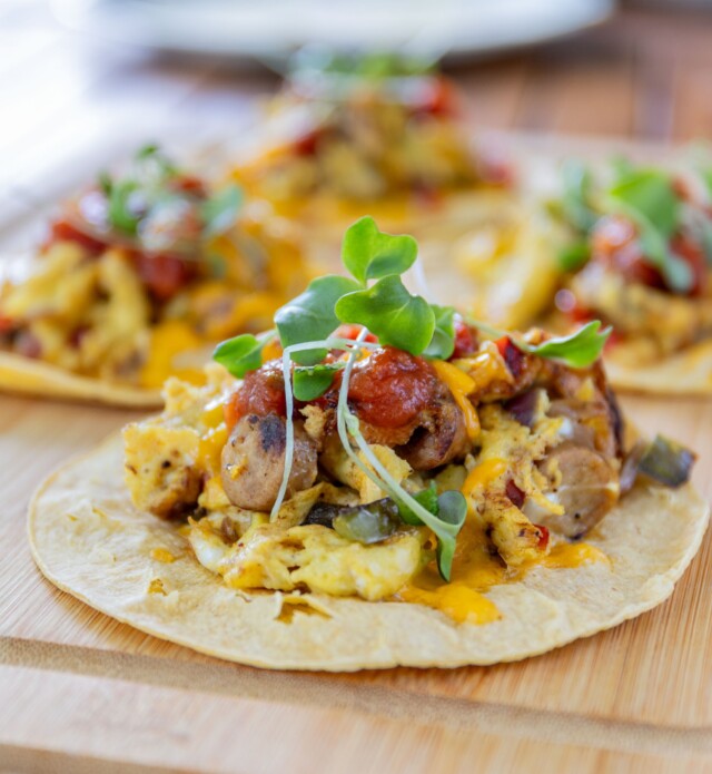 A close-up of 4 tacos plated on a wooden board.