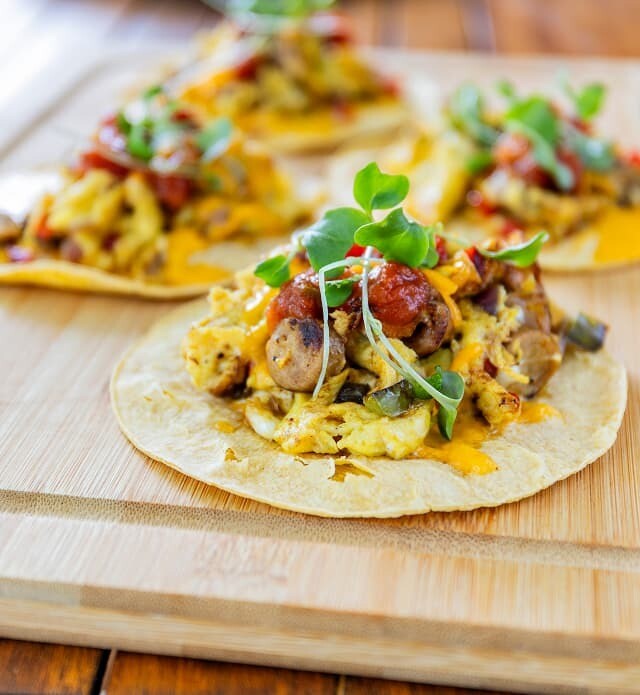 A close-up of 4 tacos plated on a wooden board.